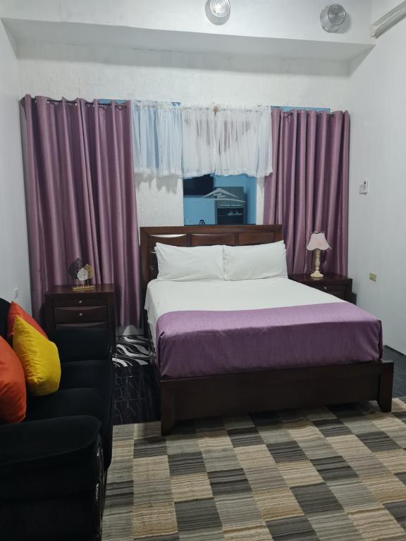 a bedroom with a bed and purple curtains and a couch at Sky Beach Rooms in Lucea