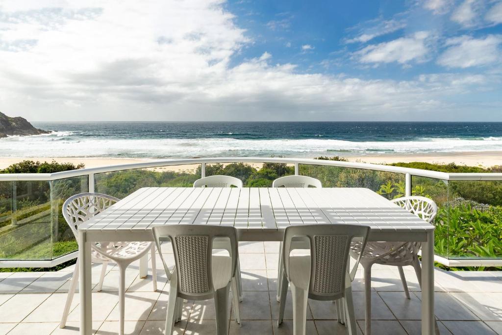 una mesa blanca y sillas en un balcón con vistas a la playa en Blue Pacific, en Blueys Beach