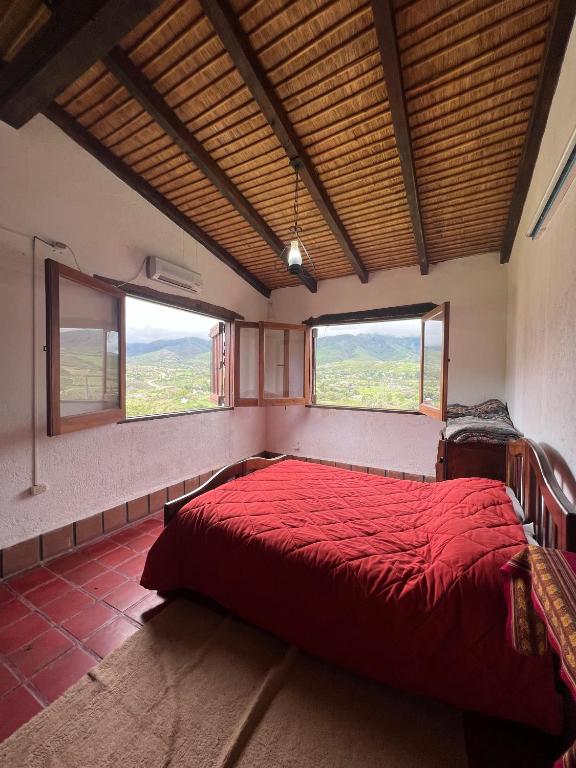 1 dormitorio con 1 cama roja y 2 ventanas en La Ramada en Tafí del Valle