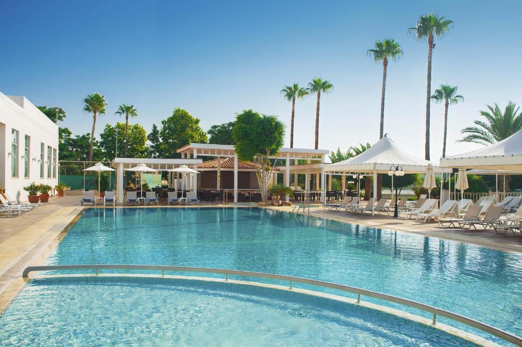 uma grande piscina com cadeiras e palmeiras em Ajax Hotel em Limassol