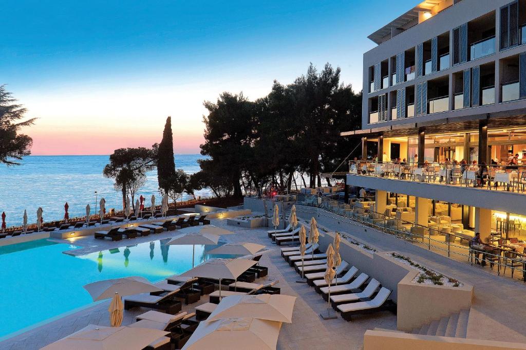 a hotel with a pool with lounge chairs and the ocean at Hotel Parentium Plava Laguna in Poreč