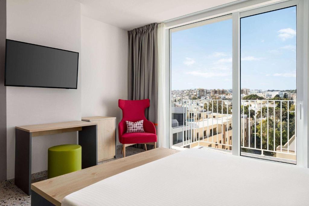 une chambre d'hôtel avec une chaise rouge et une fenêtre dans l'établissement Quadro Hotel, Trademark Collection by Wyndham, à San Ġiljan