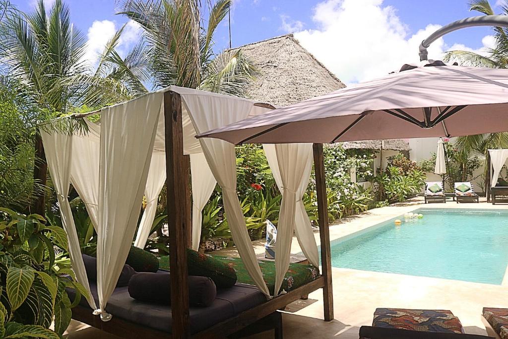 una piscina con sombrilla y una silla junto a una piscina en Aurora Boutique Hotel Jambiani en Jambiani