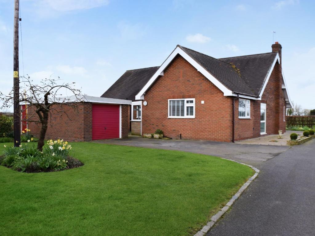 a red brick house with a red garage at Lyncroft Holiday Bungalow in Sandbach
