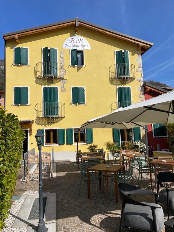 un edificio giallo con tavoli, sedie e ombrellone di Relais Fontana Rosa B&B Wellness a Caprino Veronese