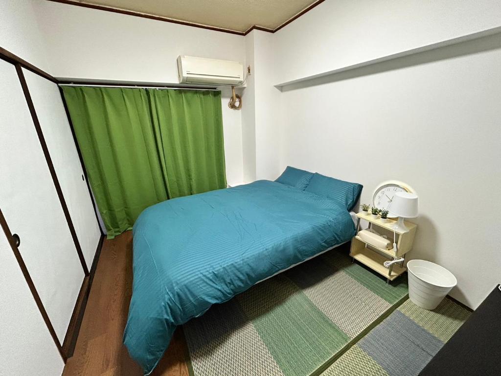 Un pequeño dormitorio con una cama azul y una cortina verde en GUEST HOUSE GREEN BASE HAKATA en Fukuoka