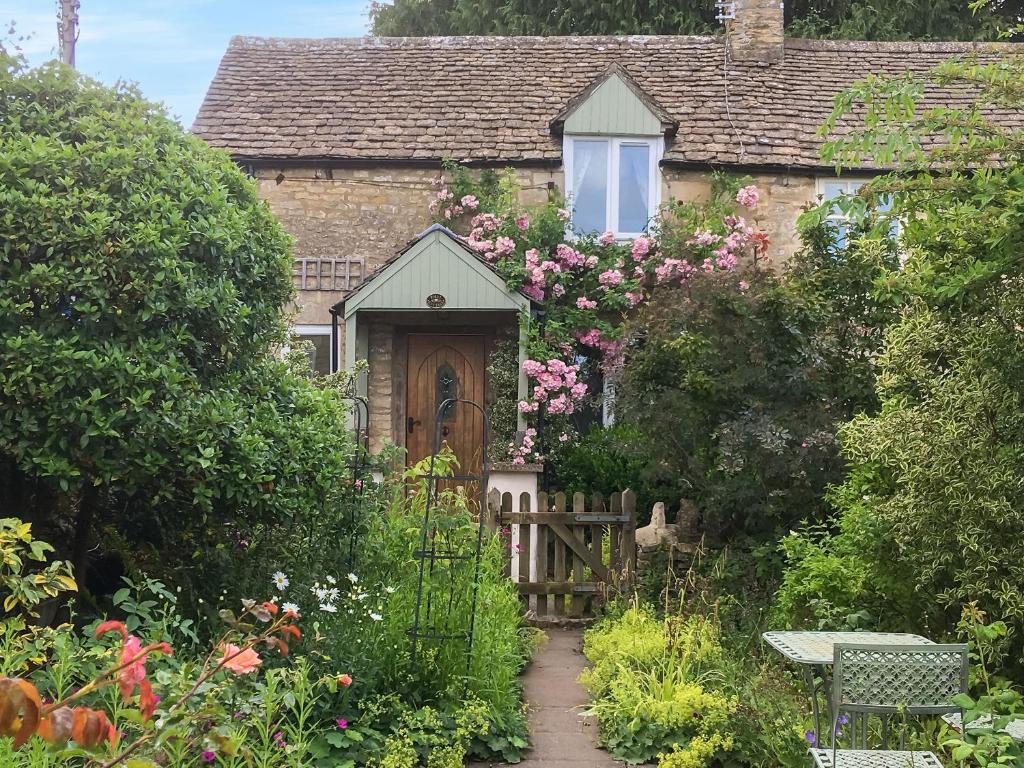 an old stone house with a wooden door and flowers at Folly Cottage in Avening