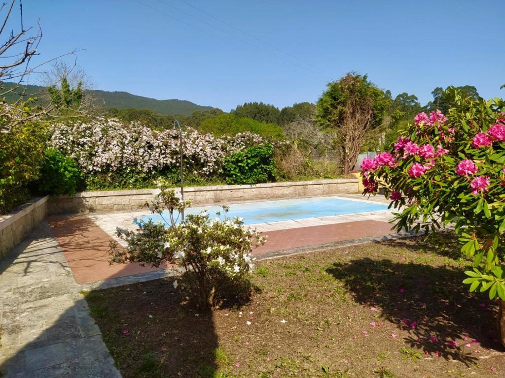 una piscina in un giardino con fiori rosa di Apartamento con jardín y piscina temporada verano privados a Samieira
