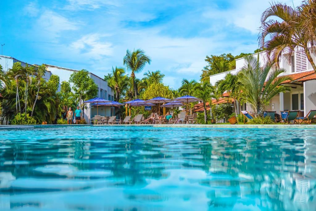 uma piscina num resort com palmeiras e guarda-sóis em Hotel Pipa Atlântico em Pipa