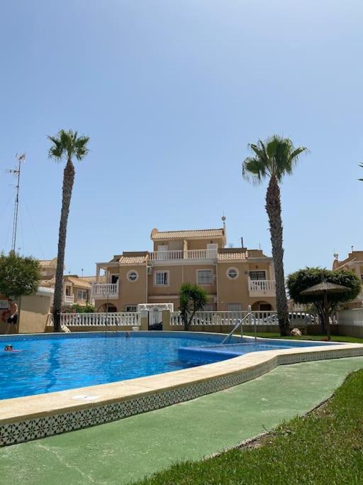a swimming pool with palm trees in front of a building at Sol Beach, Cabo Roig in Orihuela Costa