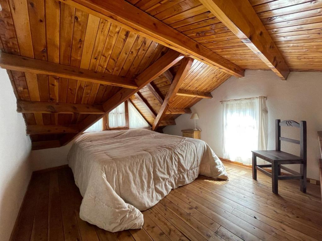 Schlafzimmer mit Holzdecken, einem Bett und einem Stuhl in der Unterkunft Casa para descansar in San Carlos de Bariloche
