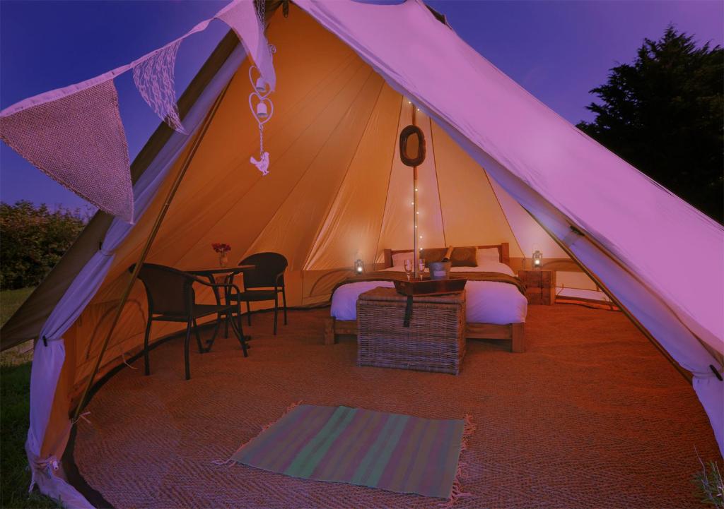 a tent with a bed and a table and chairs at Entire Glamping Site inc Dinner, Bed & Breakfast for 10 in East Chinnock