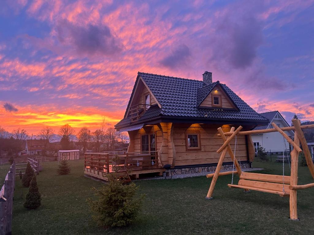 a log cabin with a swing in front of a sunset at Słoneczna Chata z Bali in Lądek-Zdrój