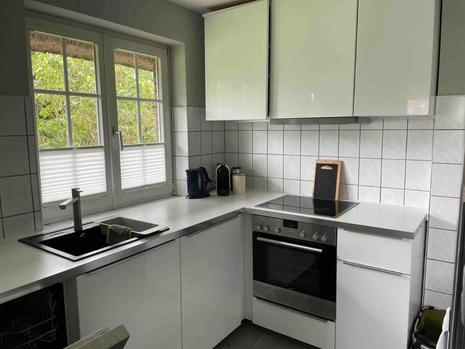 La cuisine est équipée de placards blancs, d'un évier et d'une cuisinière. dans l'établissement Kleine gemütliche Haushälfte, à Keitum