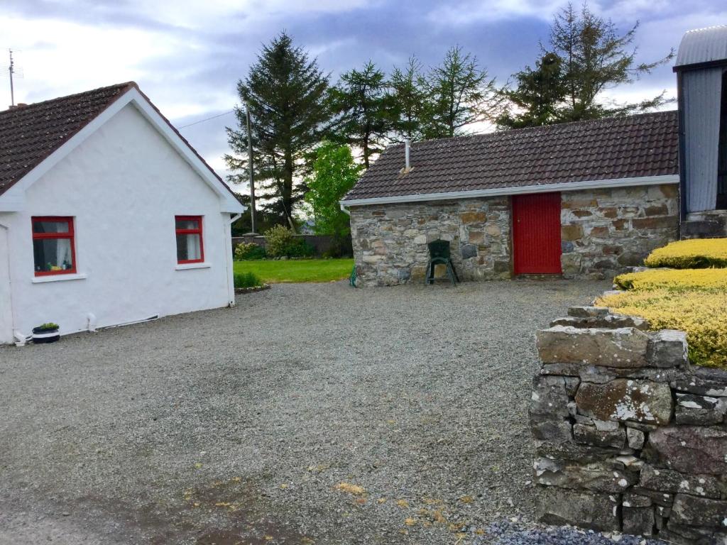 una pequeña casa blanca con una puerta roja y una entrada de grava en Mask Cottage, en Partry