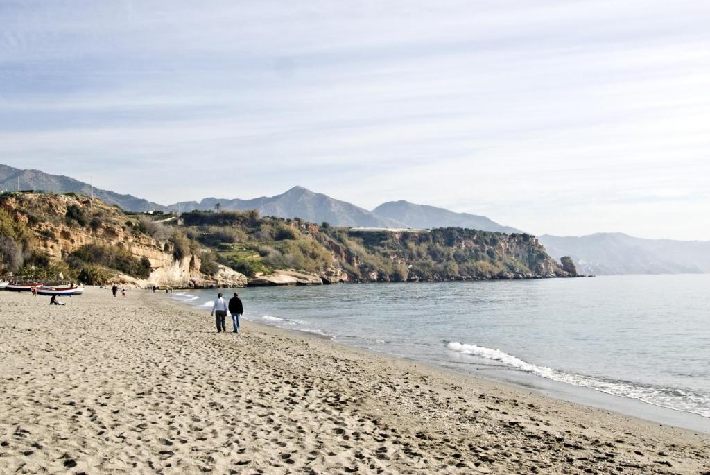 people walking on a beach with mountains in the background at Apartamentos HC Burriana Playa in Nerja