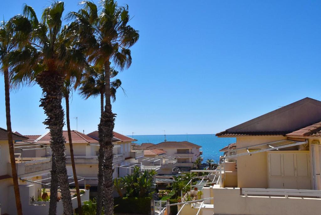 two palm trees in front of buildings and the ocean at Punta di Mola House in Marina di Ragusa