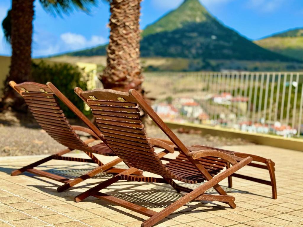 two wooden chairs sitting on a patio with a palm tree at Profetas GuestHouse in Porto Santo