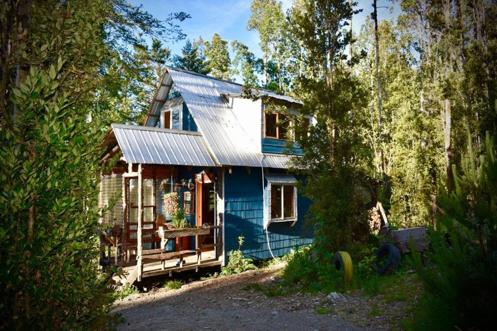 uma casa azul com um telhado prateado na floresta em Cabañas Rio Sur y tinajas calientes em Puerto Varas