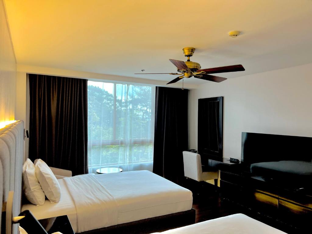Habitación de hotel con ventilador de techo y dormitorio en Forest Lodge at Camp John Hay privately owned - Deluxe Queen Suite with balcony and Parking 269 en Baguio