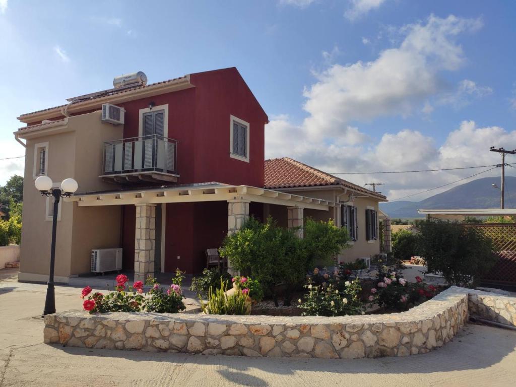 ein rotes Haus mit einem Blumenbett davor in der Unterkunft Spedion Kefallonia in Pesádha