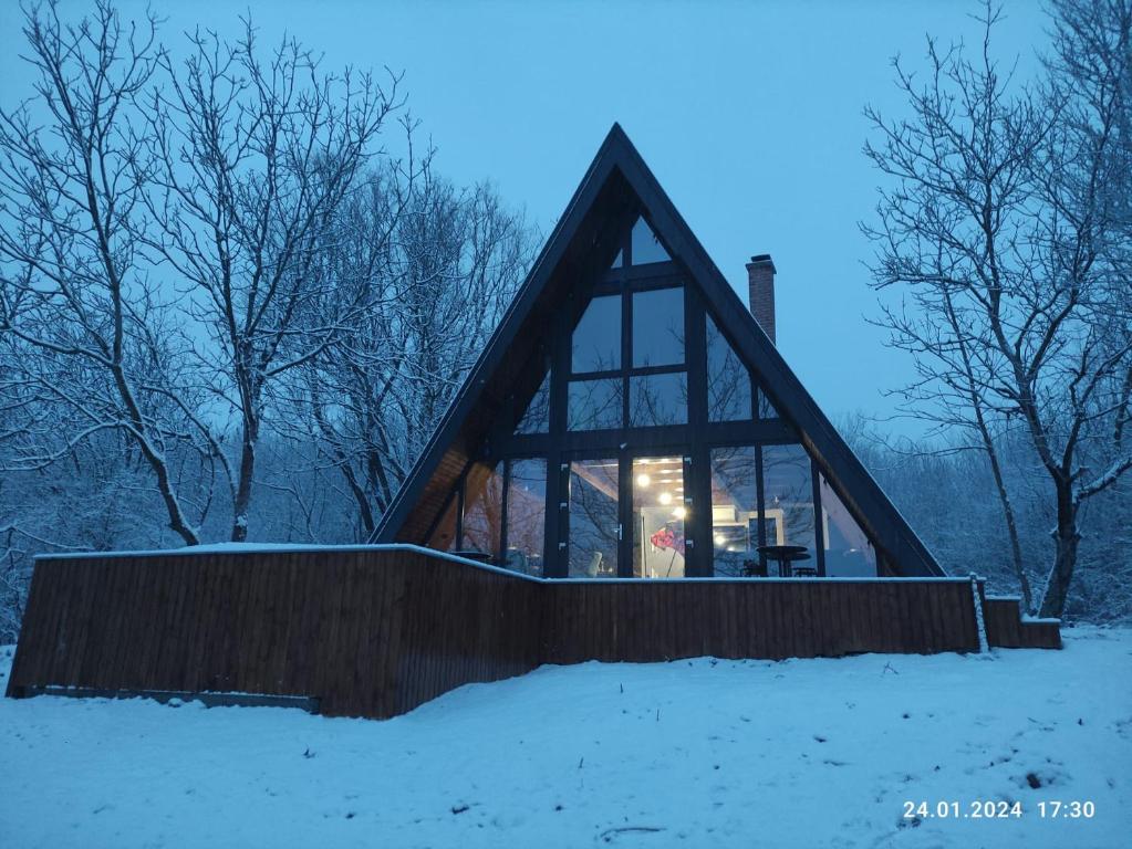 a glass house with a triangular roof in the snow at Cabana NucA-Frame in Satu Nou de Jos