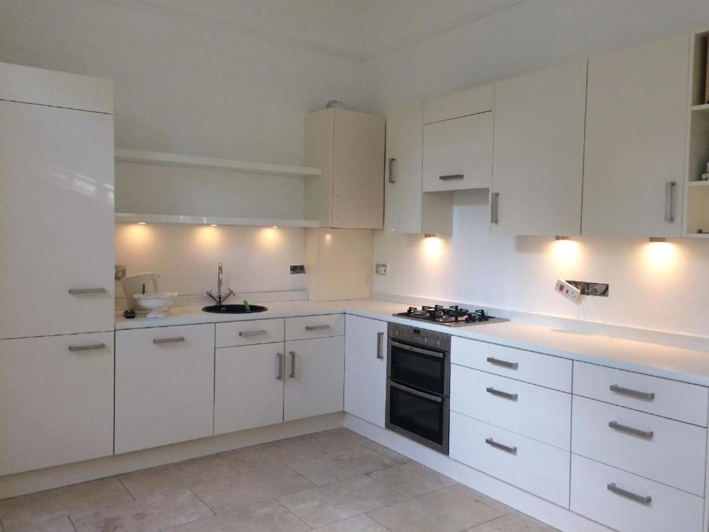una cocina blanca con armarios y electrodomésticos blancos en Ferienwohnung in einer Villa mit herrlichem Garten und Katze, en Sydenham