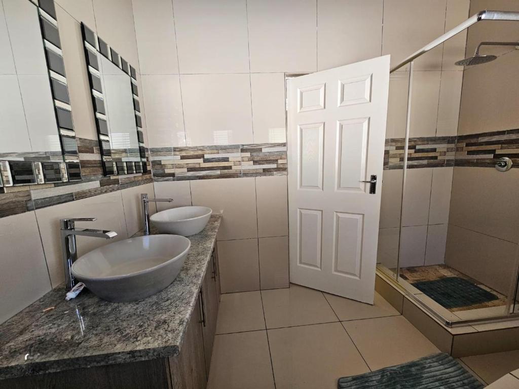 a bathroom with two sinks and a shower and a door at Omosa Guest House in Rustenburg