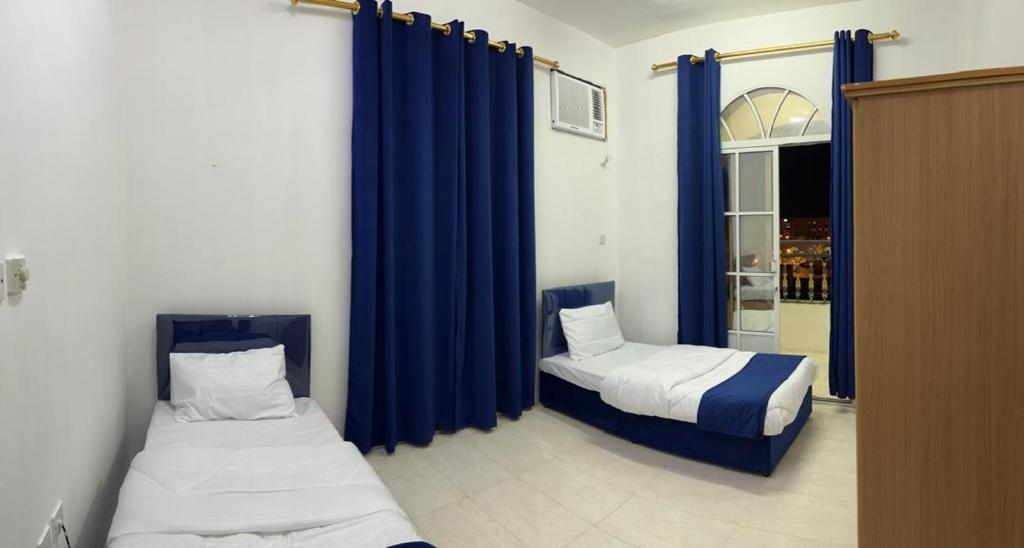 two beds in a room with blue curtains at Al Manafa Furnished Apartments in Salalah