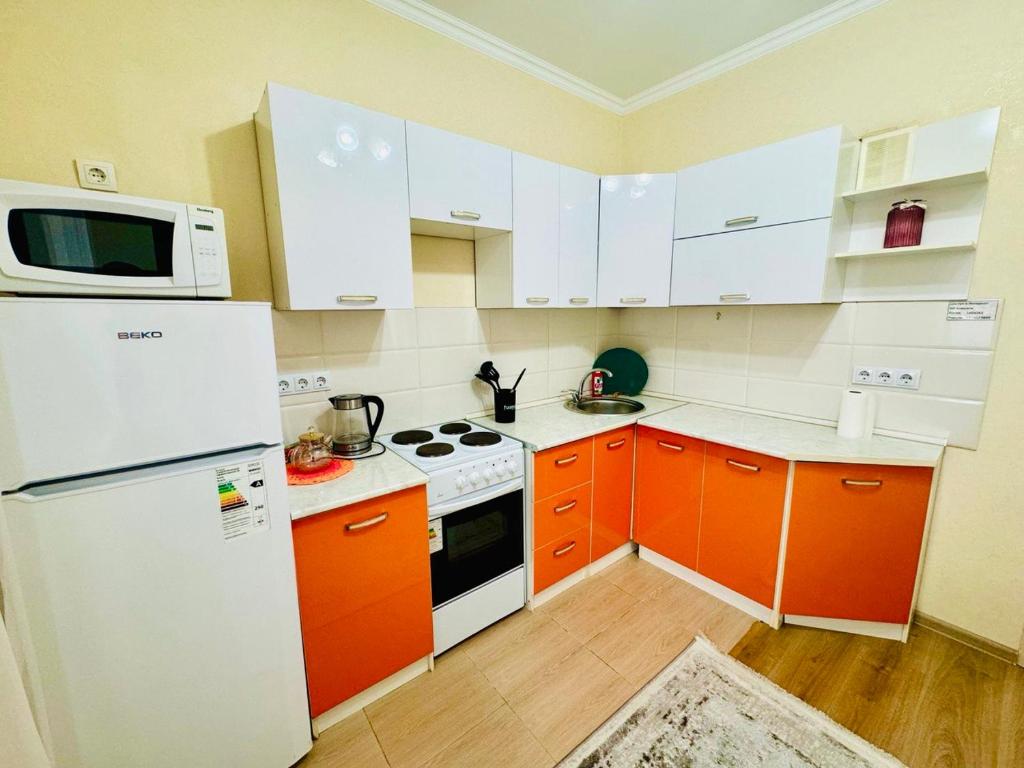 uma cozinha com armários laranja e um frigorífico branco em Уютные апартаменты в ЖК Акварель em Almaty