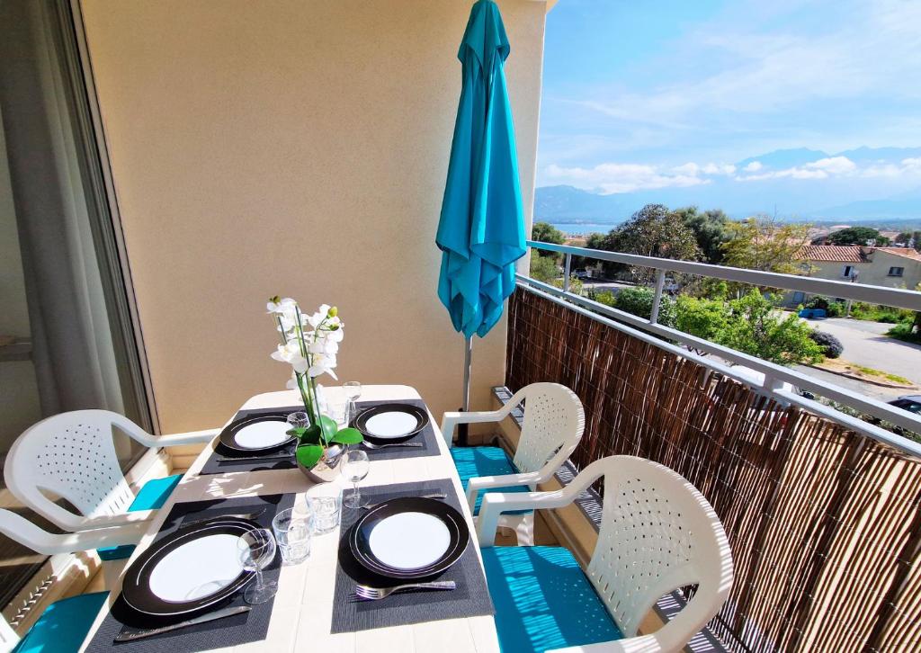 - un balcon avec une table et un parasol bleu dans l'établissement Résidence les Mimosas, à Calvi