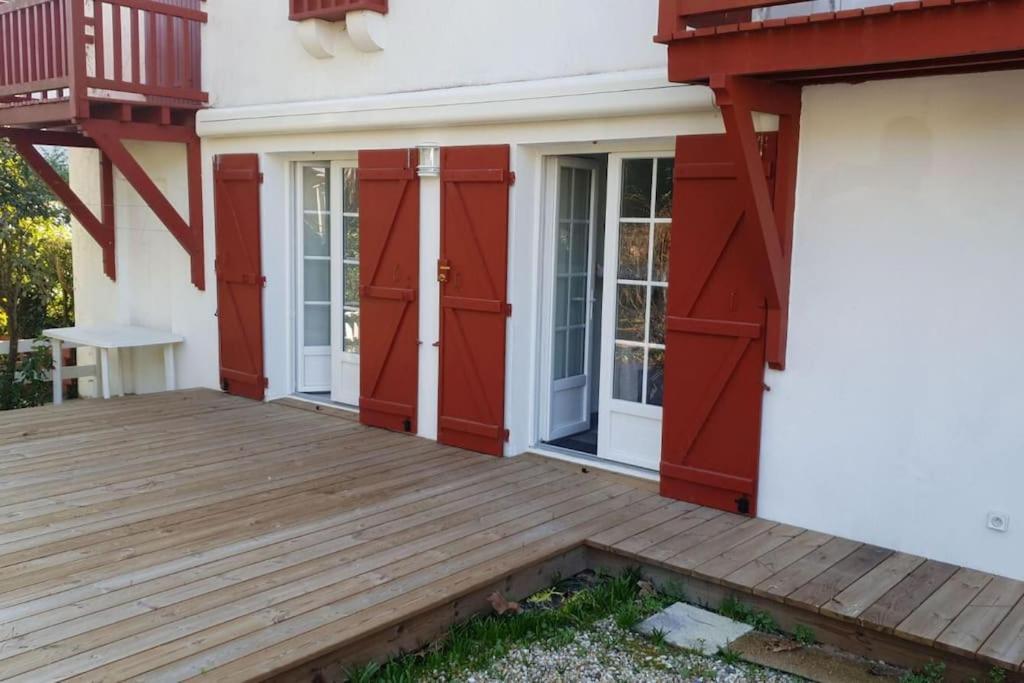 une terrasse couverte avec des portes rouges et une terrasse en bois dans l'établissement Appartement 2 chambres avec jardinet privatif - 200m de la plage Pereire, à Arcachon