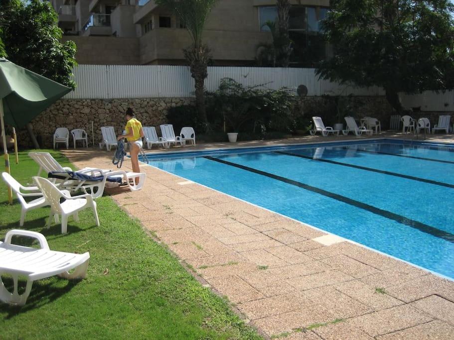 a woman walking next to a swimming pool with chairs and a person walking by at Herzliya Pituach Apartment with Pool, by the Beach in Herzliya