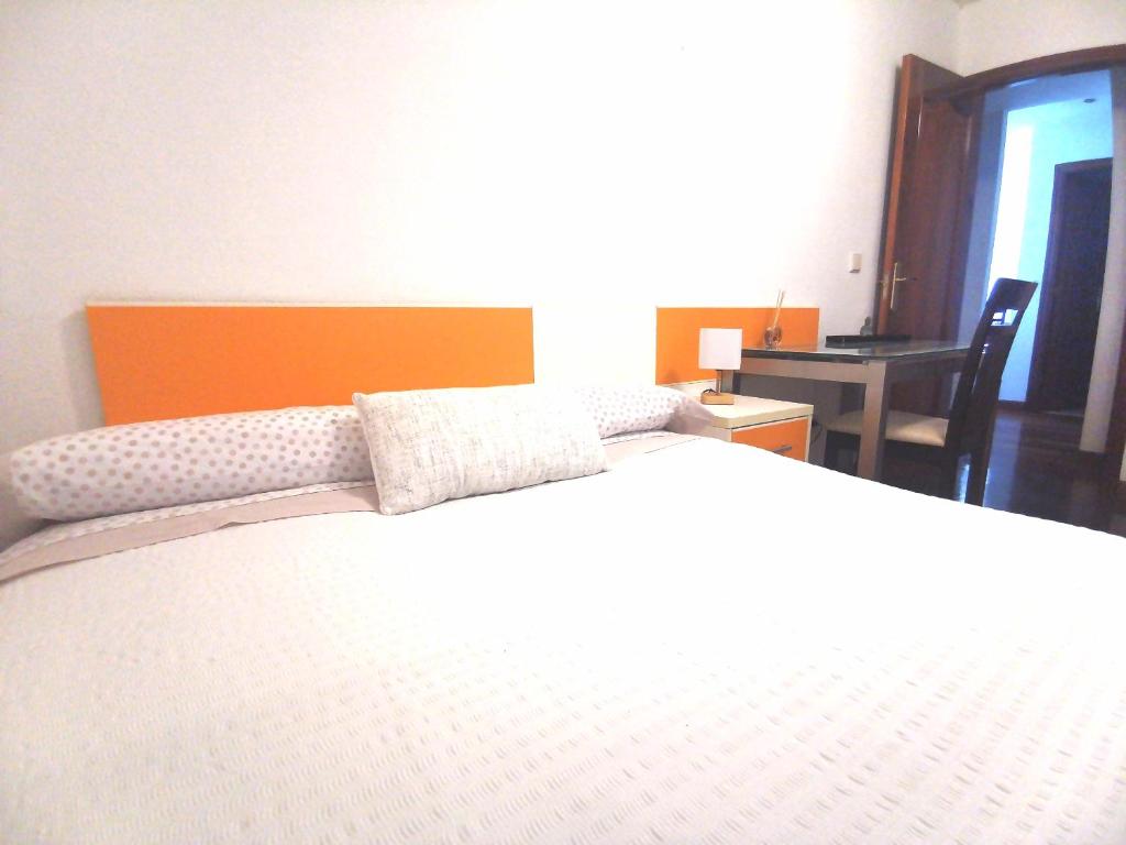 una camera da letto con un grande letto bianco con testiera arancione di Habitación cerca del aeropuerto a Maliaño