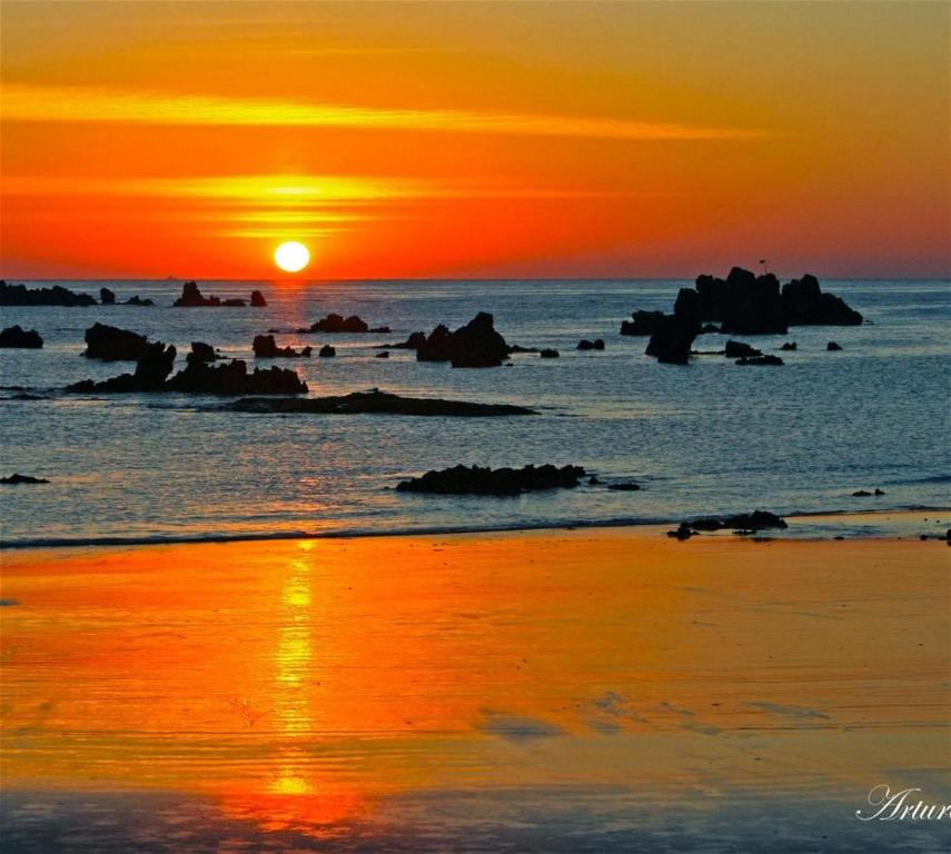 einen Sonnenuntergang über dem Meer mit Felsen im Wasser in der Unterkunft Hotel Arillo in Noja
