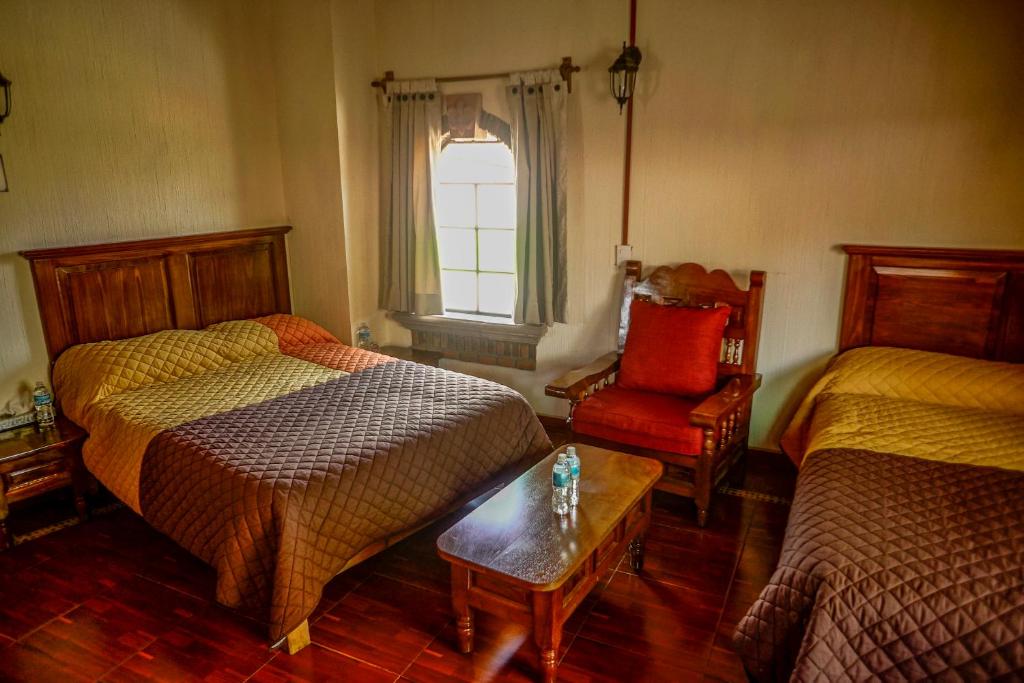 a bedroom with two beds and a chair and a window at Hotel Villas San Miguel in Pátzcuaro