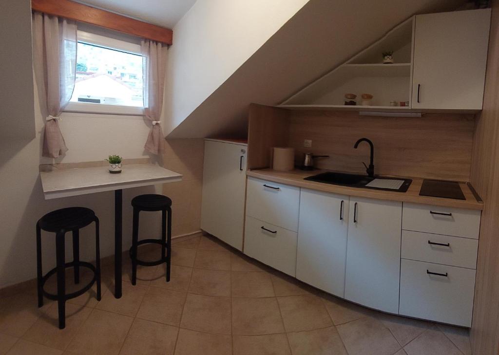 una cocina con armarios blancos, fregadero y taburetes en Guesthouse Anita, en Kotor