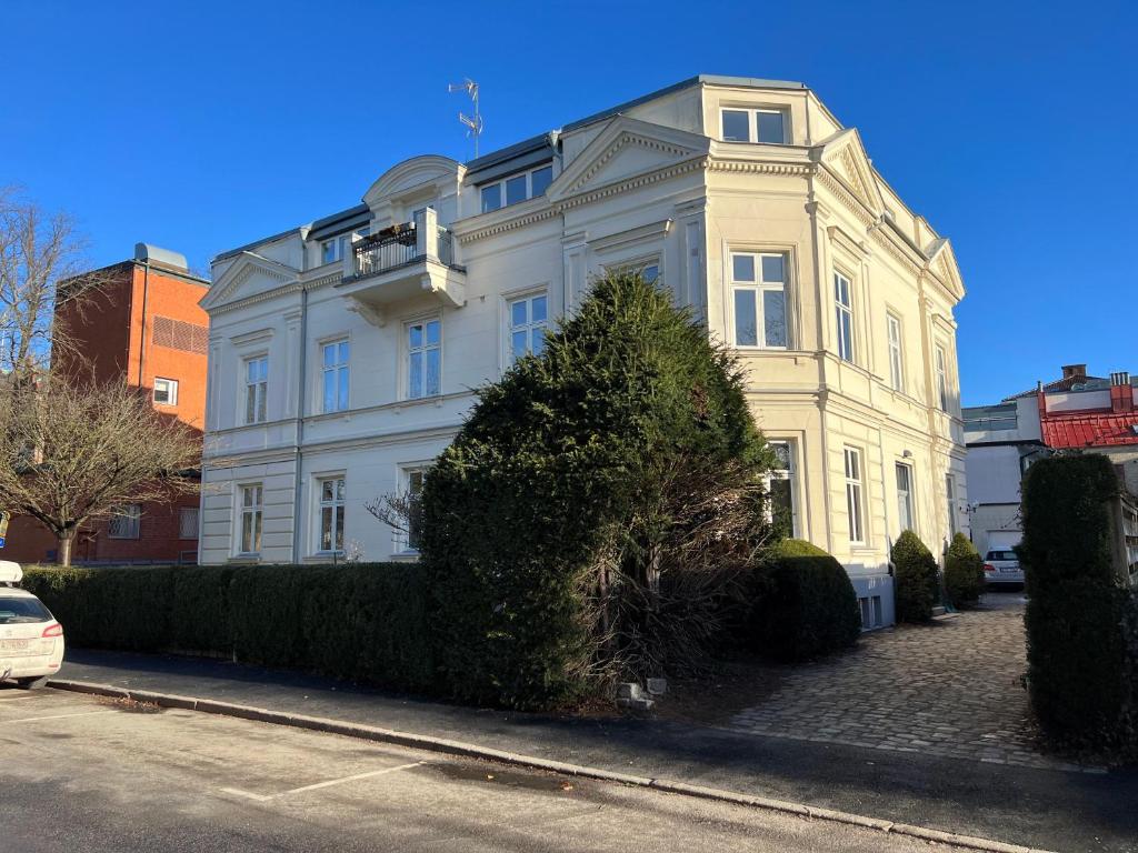 a white house on a street with a hedge at Elegant lägenhet i Professorstaden in Lund