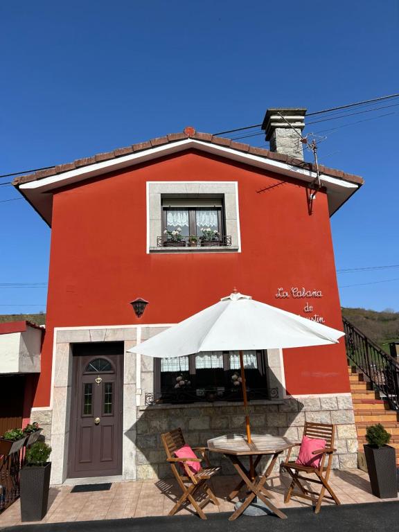 a red building with a table with an umbrella at La Cabaña de Agustin in Ortiguero