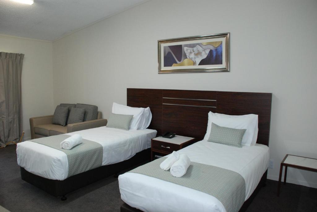a hotel room with two beds and a chair at Auckland Airport Kiwi Motel in Auckland