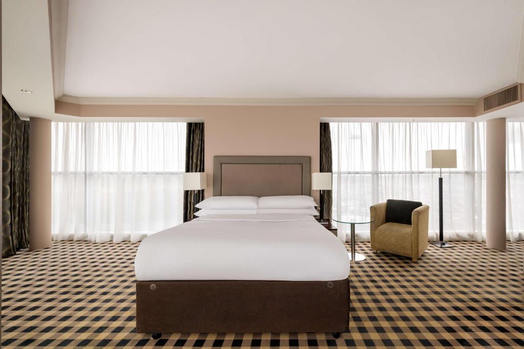 a bedroom with a bed and a chair and windows at DoubleTree by Hilton Hotel Newcastle International Airport in Newcastle upon Tyne