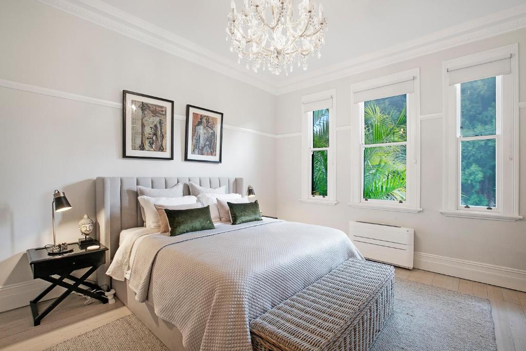 a white bedroom with a bed and a chandelier at Beautiful victorian garden apartment, with pool. in Sydney
