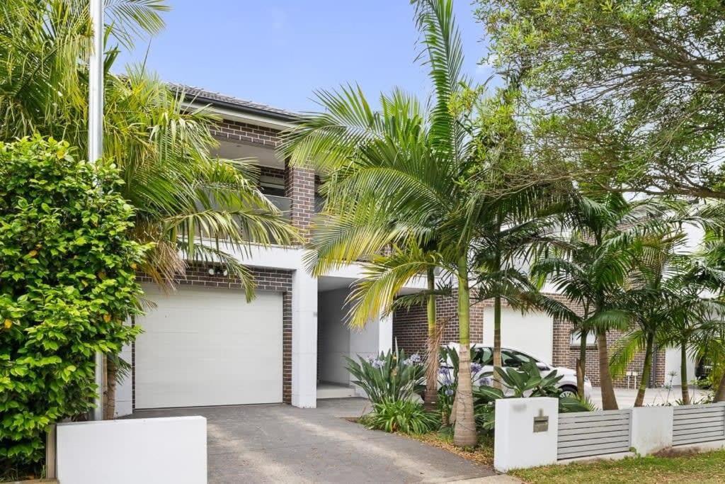 a house with white garage doors and palm trees at Lovely 4 Bedroom 3 Bathroom Modern Home Sleeps 8 in Revesby