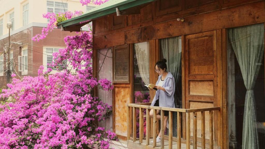 a woman standing on a balcony looking at a book at Utopia Homestay Đà Lạt in Khu Chi Lăng