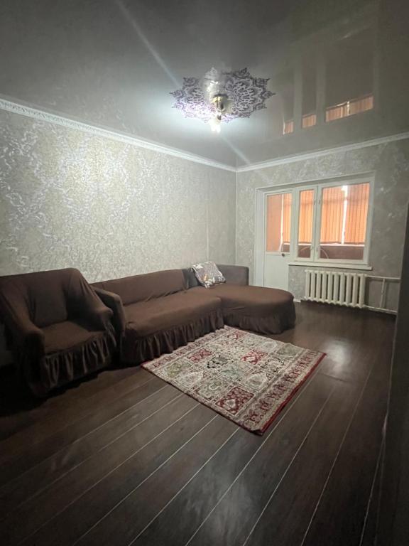 een woonkamer met een bruine bank en een tapijt bij Квартира in Simkent
