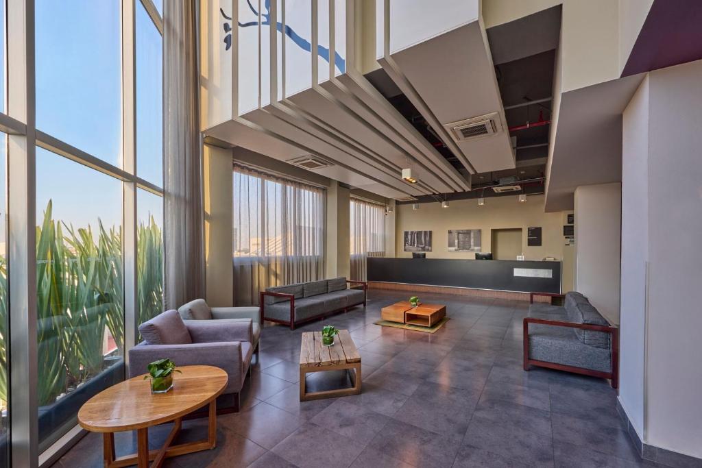 A bright, high-ceilinged lounge leads toward the reception desk, with sofas and armchairs along a wall of windows.