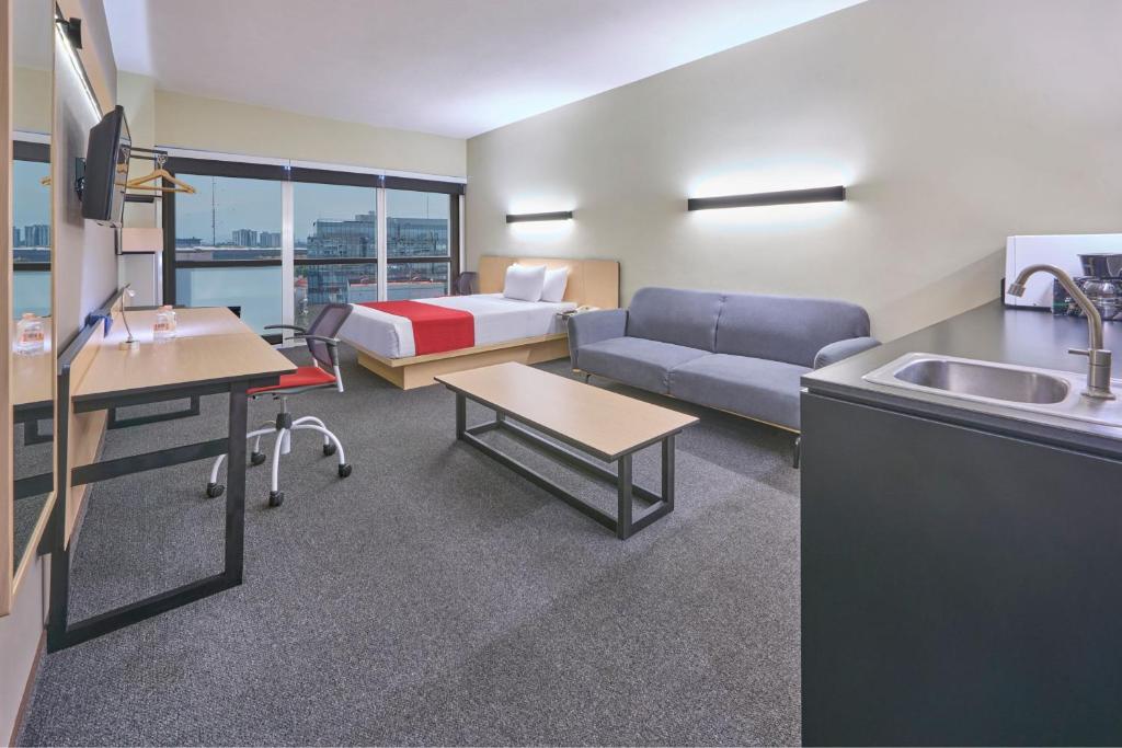 A spacious room combining a bed, sofa, desk and exposed sink area.