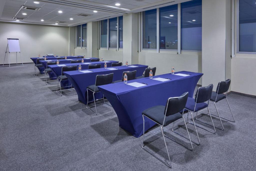 A long event room set with blue tables, chairs and a presentation board.