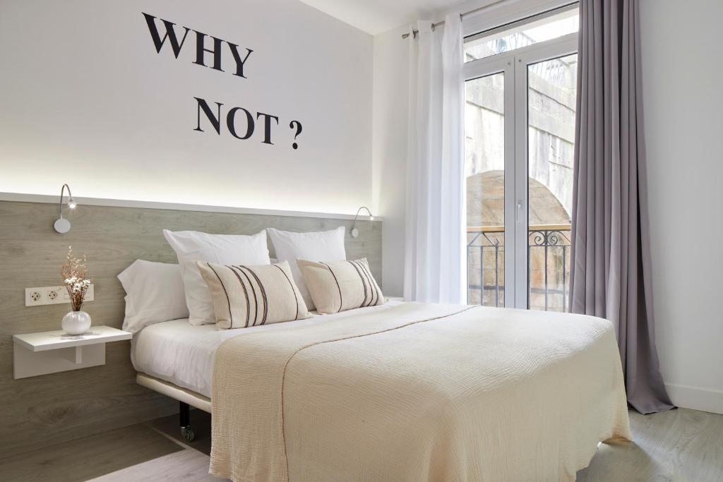 a white bedroom with a bed with a why not sign on the wall at Pension El Puerto in San Sebastián