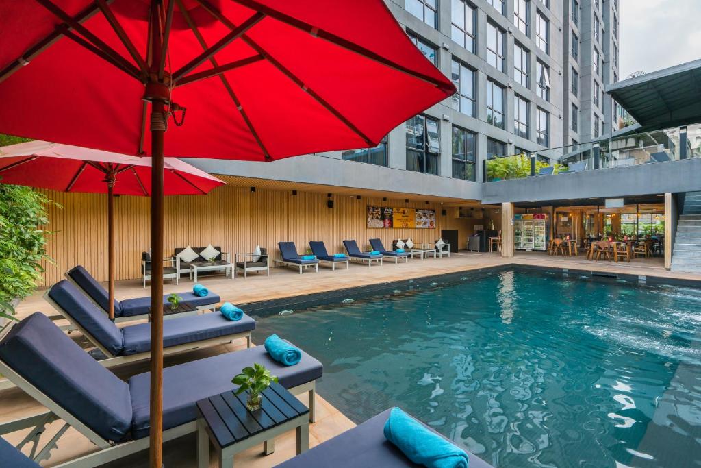 a pool with a red umbrella and chairs and a building at Galleria 12 Sukhumvit Bangkok by Compass Hospitality in Bangkok